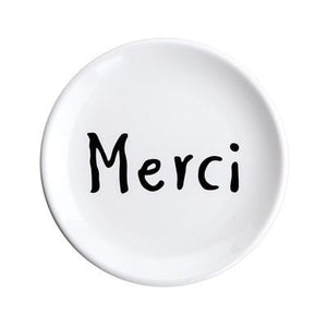 The word Merci printed in black on a white ceramic plate