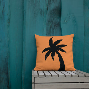 orange colour cushion cover with a black palm tree print placed outside a blue wooden wall