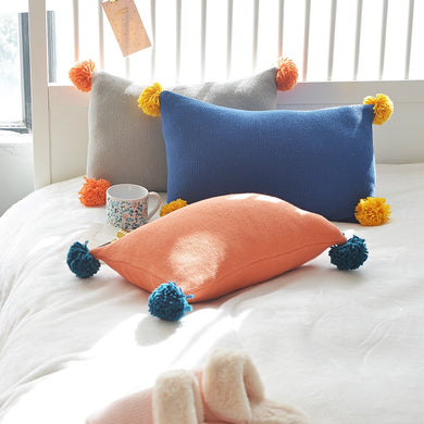3 cushion covers in grey, blue and orange lying on a bed