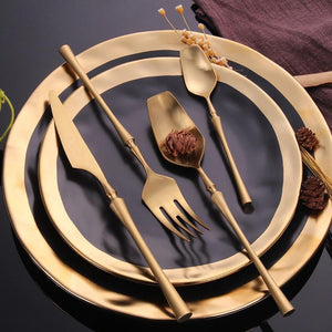 GOLD PLATED ROYALTY CUTLERY SET SITTING ON TOP OF A BLACK PLATE WITH GOLD TRIMMED EDGES