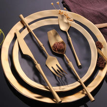 Load image into Gallery viewer, GOLD PLATED ROYALTY CUTLERY SET SITTING ON TOP OF A BLACK PLATE WITH GOLD TRIMMED EDGES