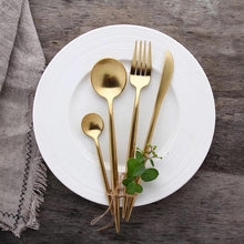 Load image into Gallery viewer, Classy Ains Gold-plated cutlery set with large and small sized spoons, fork and knife resting with decoration on a white plate