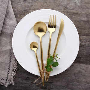 Classy Ains Gold-plated cutlery set with large and small sized spoons, fork and knife resting with decoration on a white plate